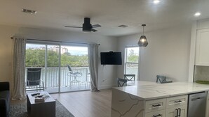 Una cocina moderna con una isla de mármol, armarios blancos y un televisor de pantalla plana.
