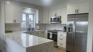 Una cocina moderna con armarios blancos, encimera de mármol, electrodomésticos de acero inoxidable y un ventanal que proporciona luz natural.