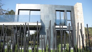 Un edificio moderno con fachada de vidrio, una torre de piedra y un balcón con barandillas de metal.
