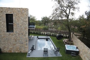 A modern outdoor pool area with stone walls, lounge chairs, and a hot tub.