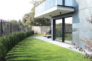 A modern building with a glass facade, a stone wall, and a neatly trimmed lawn.