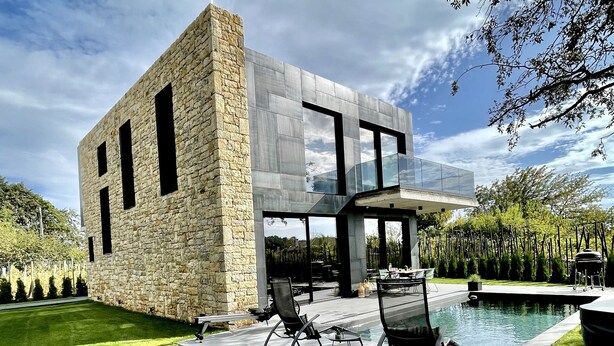 Una casa moderna con fachada de piedra, un invernadero de cristal y una piscina.