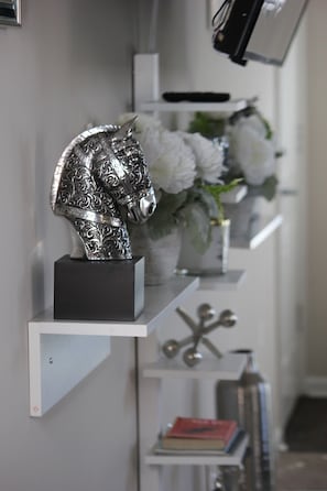 A silver decorative horse head sculpture on a white shelf, surrounded by white flowers and books.