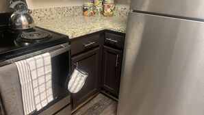 A kitchen with a stove, oven, and refrigerator. There are three jars on the counter and a kettle on the stove.