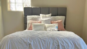 A neatly made bed with a grey headboard, white bedding, and several decorative pillows.