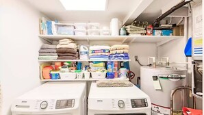 A laundry room with two front-loading washing machines, shelves with folded towels, and various cleaning supplies. - Margaritaville, Steps From The Snook Inn, Olde Marco (Marco Island)