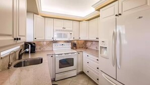 A kitchen with white cabinets, a built-in microwave, a stove, a sink, and a refrigerator. - Margaritaville, Steps From The Snook Inn, Olde Marco (Marco Island)