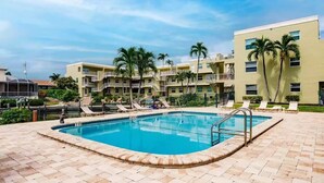 A swimming pool surrounded by lounge chairs and palm trees, with a multi-story building in the background. - Margaritaville, Steps From The Snook Inn, Olde Marco (Marco Island)