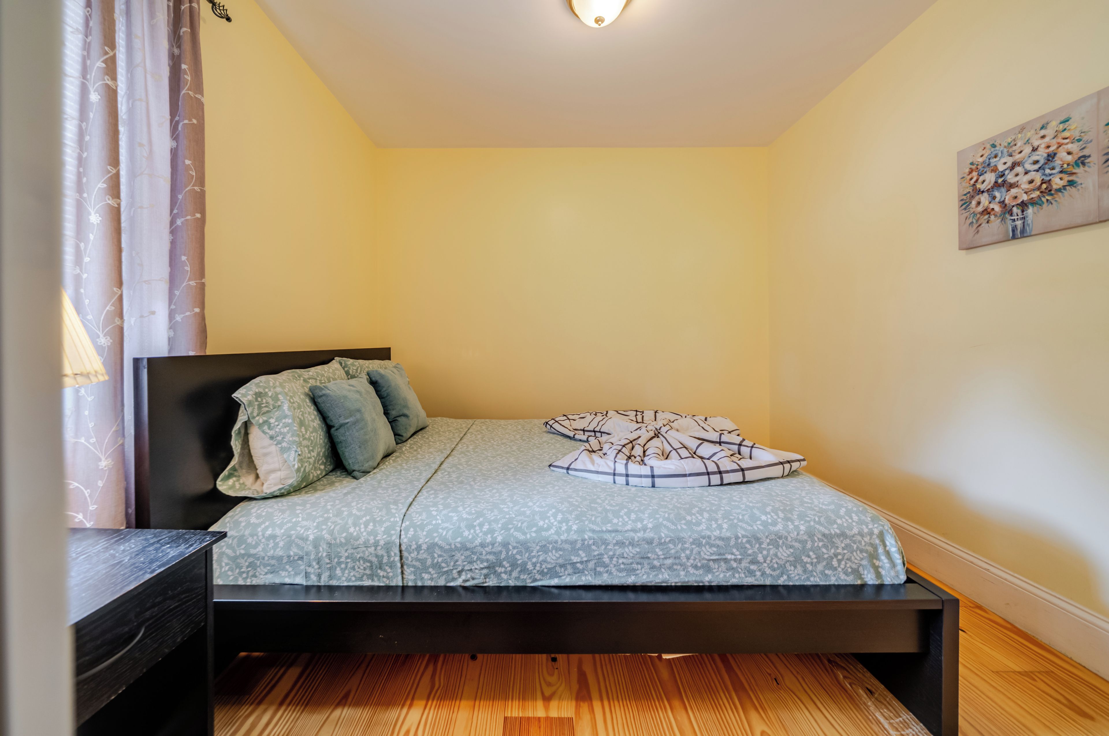 A single bed with a headboard, a bedside table, and a wall-mounted painting.