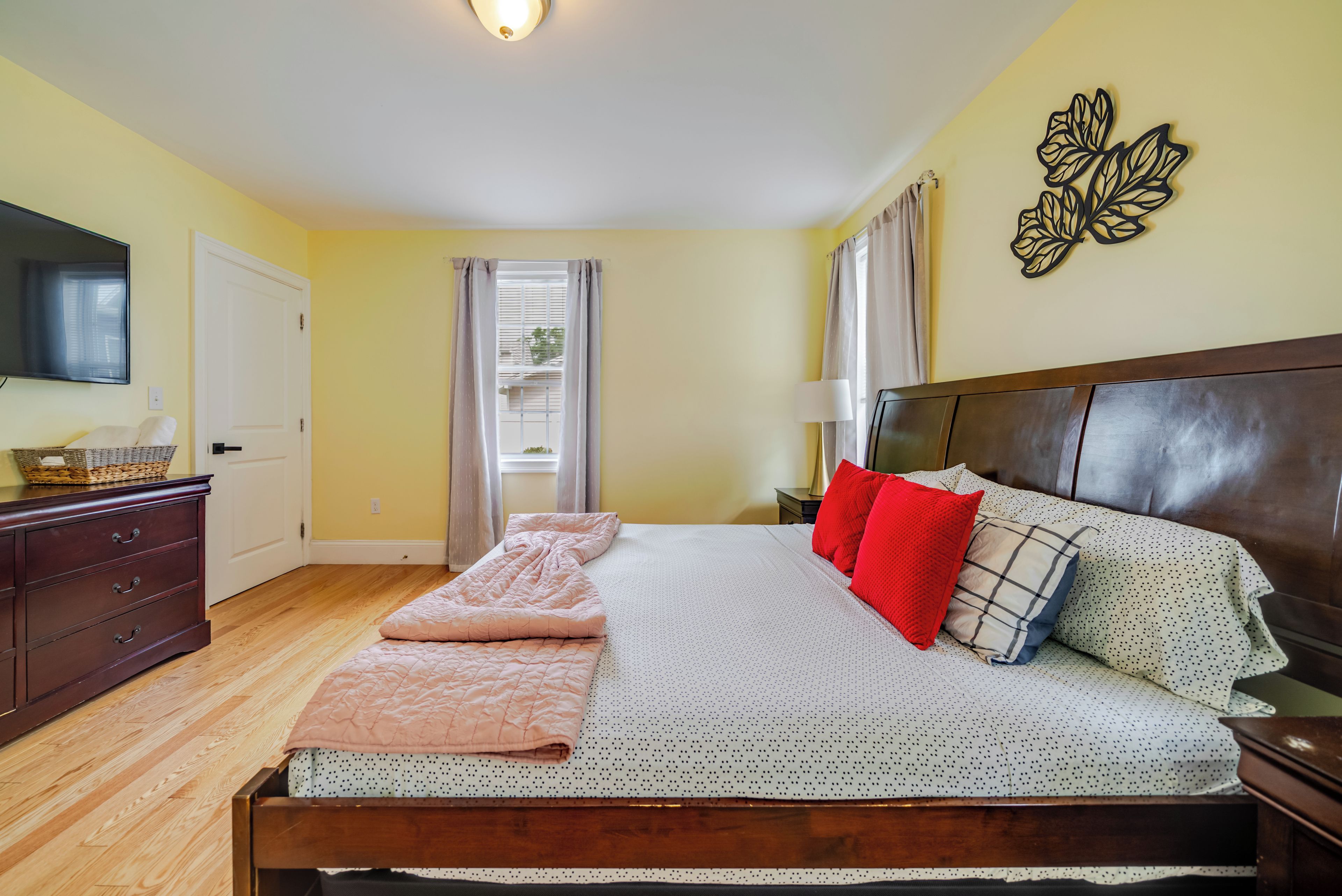 Een slaapkamer met een bed, een dressoir, een televisie en een raam met gordijnen.