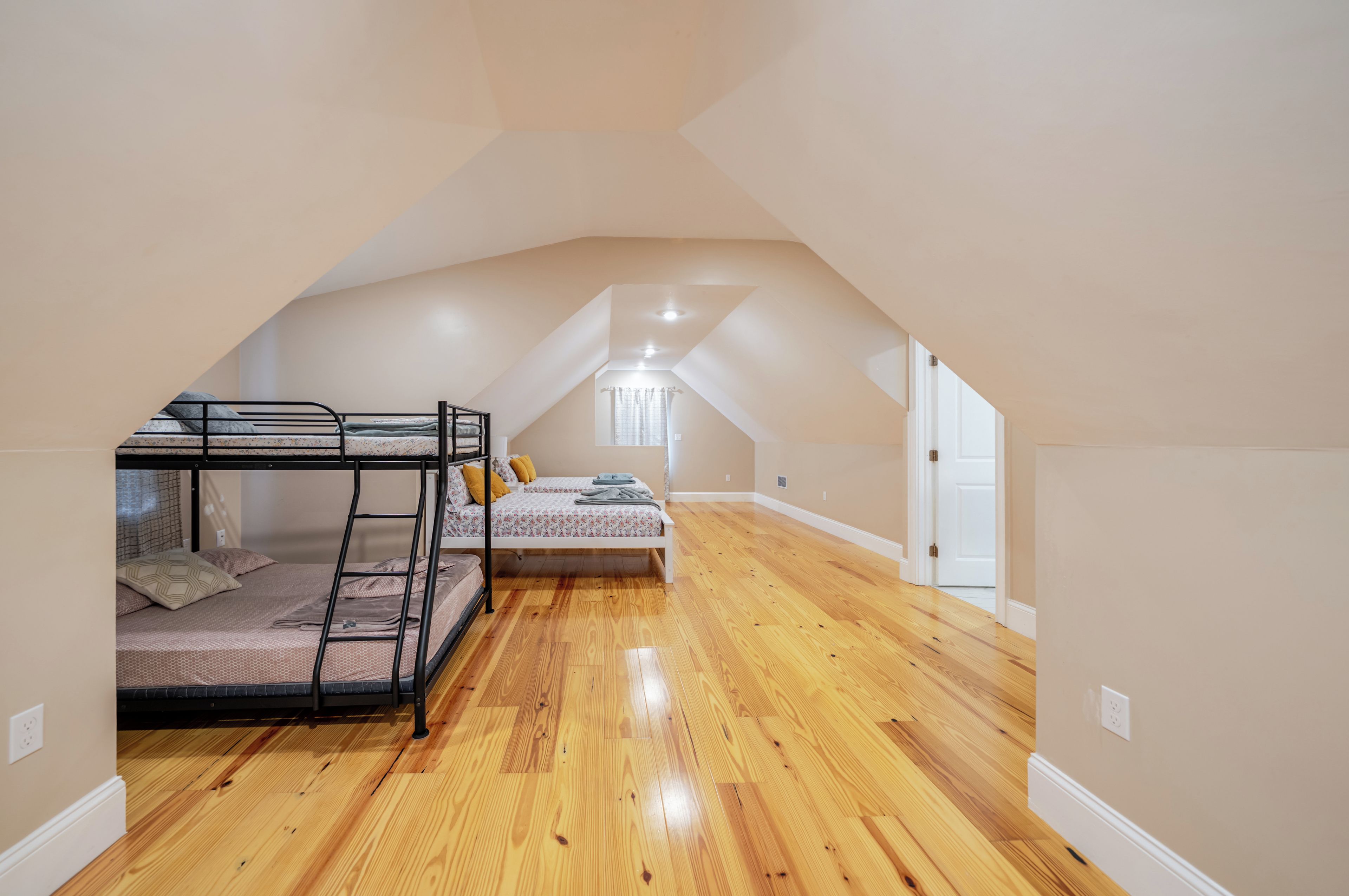 A room with a bunk bed, a single bed, wooden flooring, and a sloped ceiling.