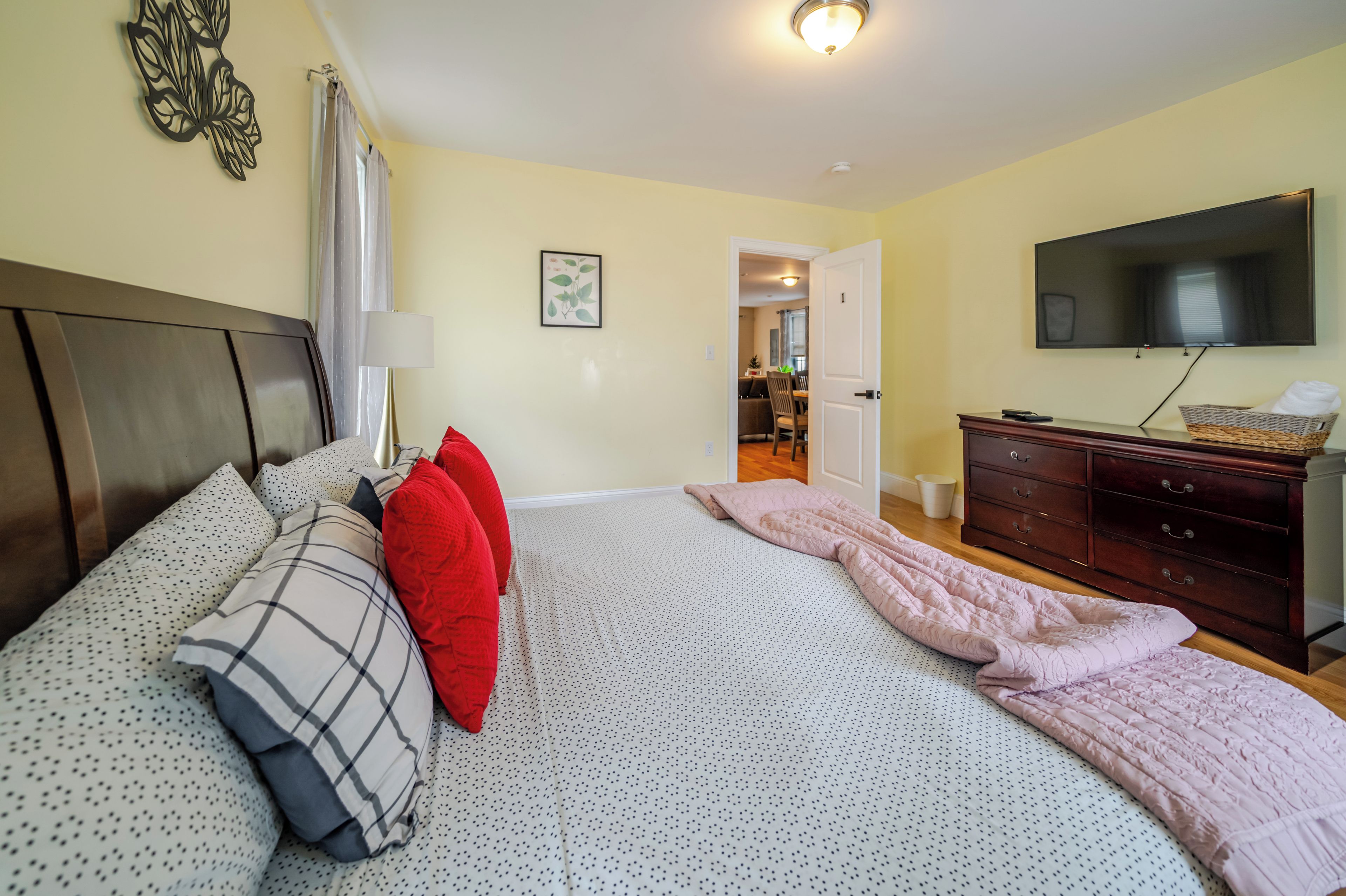 Un dormitorio con cama, cómoda, televisor y puerta que da a otra habitación.