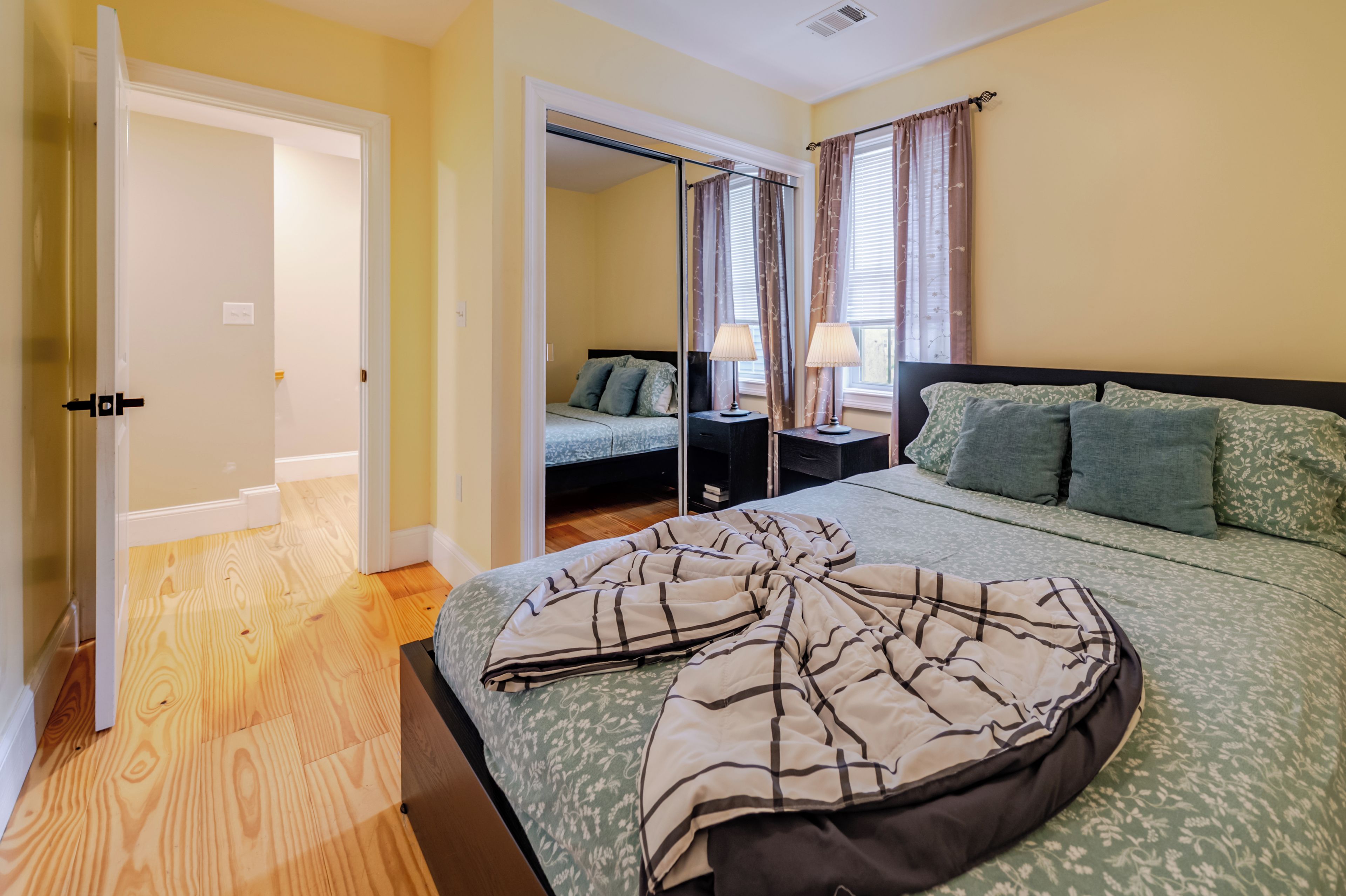 Un dormitorio con cama, mesitas de noche, un espejo y una ventana con cortinas.