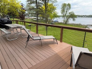 A deck with a grill, lounge chairs, and a view of a lake.