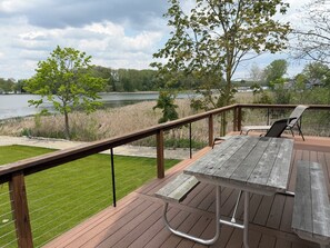 A wooden deck with a picnic table and chairs overlooking a lake. - The Cheerful Lake House at Crane Cove (Jackson)