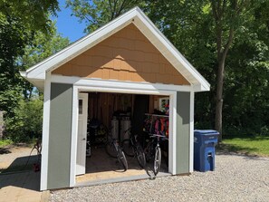A small shed with a door open, revealing bicycles and storage items inside.