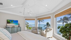 Une chambre avec un grand lit, un ventilateur de plafond, une télévision, une commode et une vue sur l’océan.
