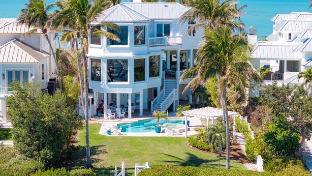 Une maison à plusieurs étages avec une piscine, entourée de palmiers et offrant une vue sur l’océan.