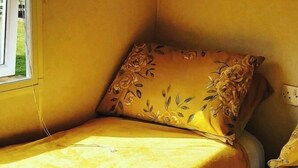 Pieni huone, jossa on yksi sänky, keltainen päiväpeite ja kukkakuviollinen koristetyyny.