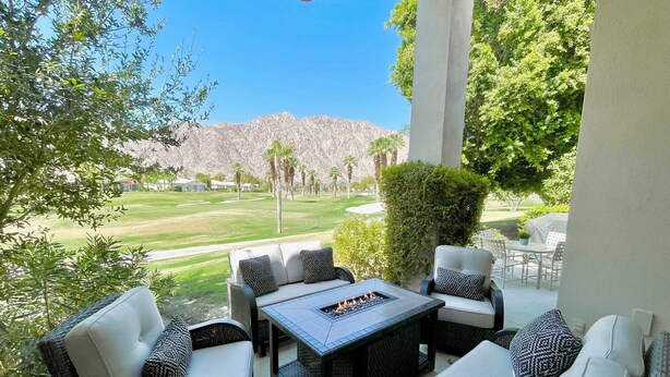 Eine Terrasse im Freien mit Korbmöbeln, einer Feuerstelle und Blick auf einen Golfplatz.