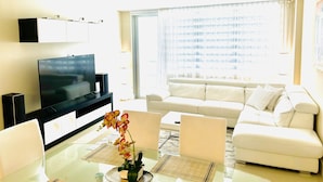 A modern living room with a flat-screen TV, white sofa, and a glass dining table with chairs. - 97-B Free Parking! Beautiful Oceanfront Condo! (Hollywood)