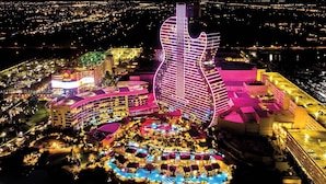 A large hotel with a distinctive guitar-shaped building, multiple swimming pools, and a well-lit outdoor area. - 97-B Free Parking! Beautiful Oceanfront Condo! (Hollywood)