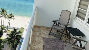 A balcony with two chairs and a small table, overlooking a beach with palm trees and the ocean. - 97-B Free Parking! Beautiful Oceanfront Condo! (Hollywood)