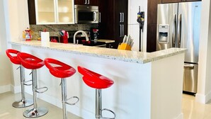 A modern kitchen with dark wooden cabinets, stainless steel appliances, a marble countertop, and three red bar stools.