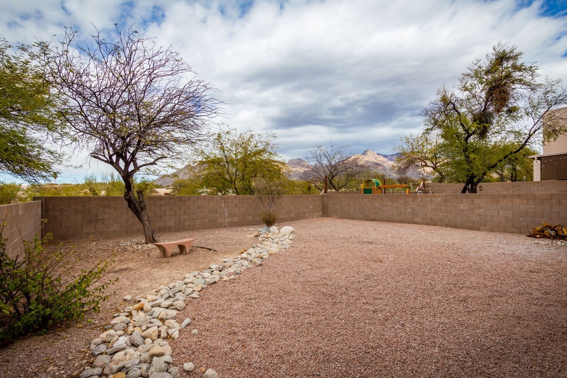 A backyard with a gravel area, a brick wall, and a small bench.