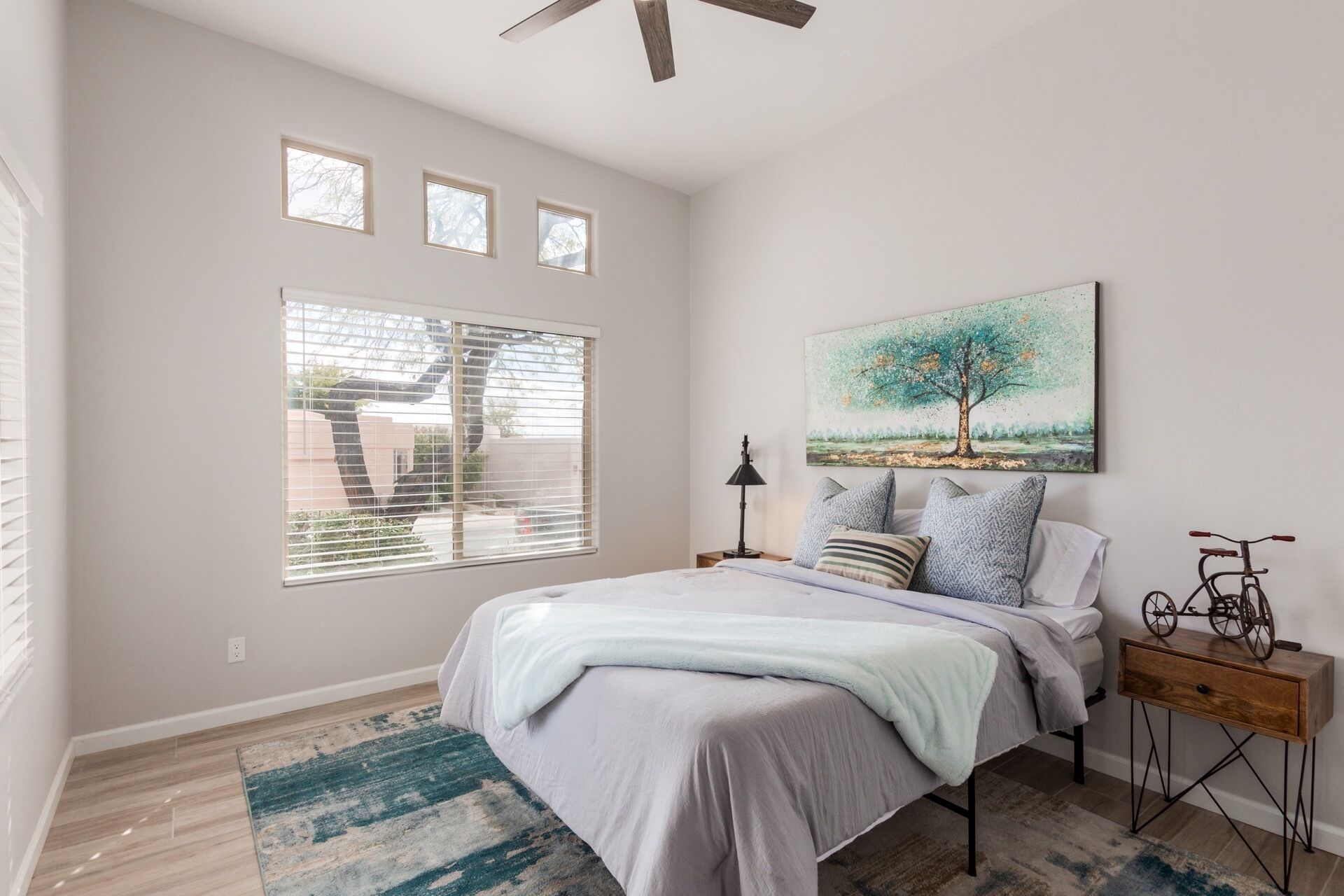 A bedroom with a bed, a nightstand, a lamp, a painting, and a bicycle on a side table.