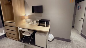 A compact hotel room with a wooden desk, a chair, a small refrigerator, a TV mounted on the wall, and a wardrobe. - Contractor Accommodation - Cacco (Corby)