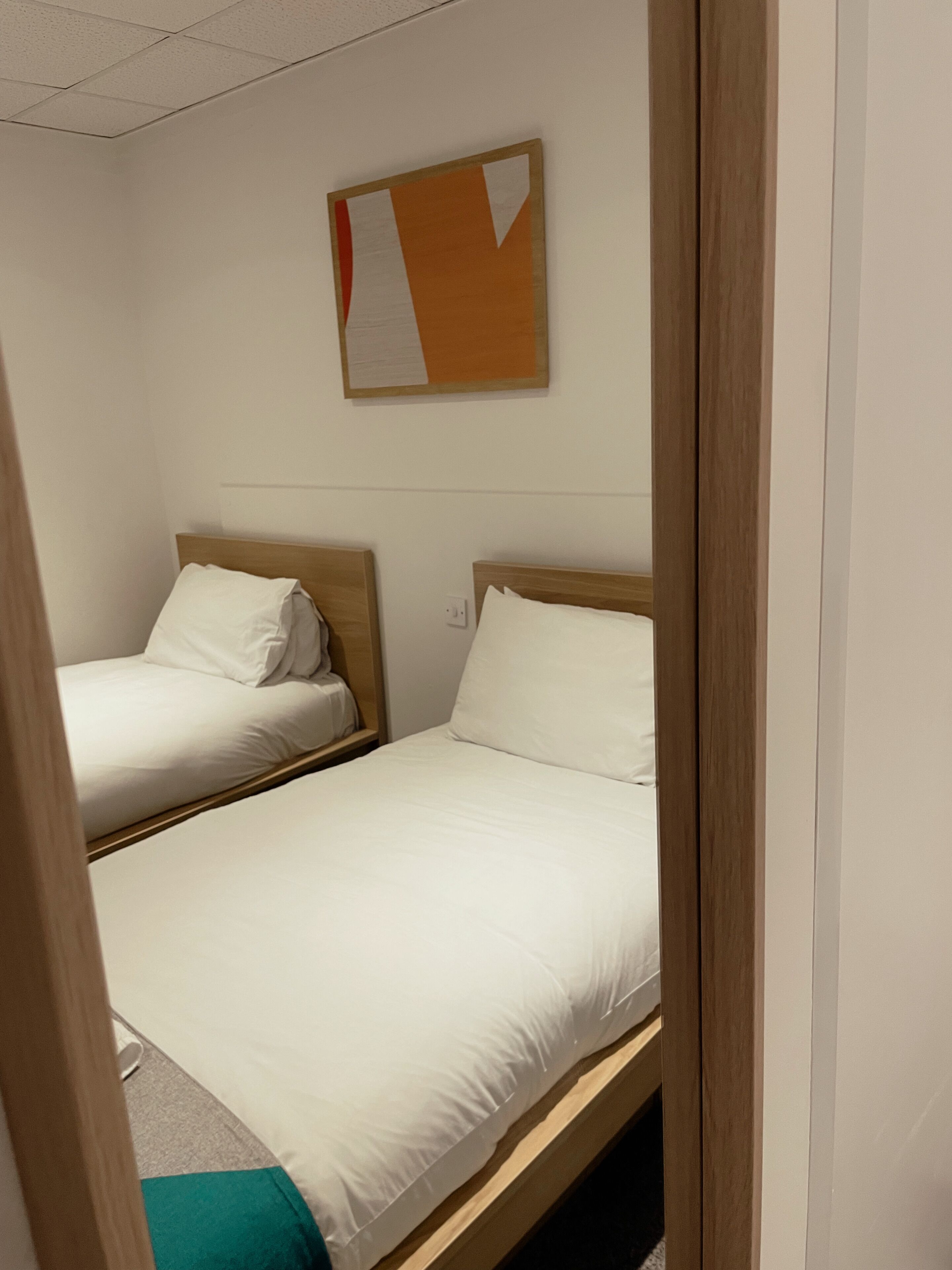 A hotel room with two single beds, wooden headboards, white bedding, and a wall-mounted artwork.