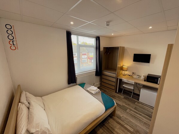 A hotel room with a bed, a desk, a chair, a TV, and a window with curtains. - Contractor Accommodation - Cacco (Corby)