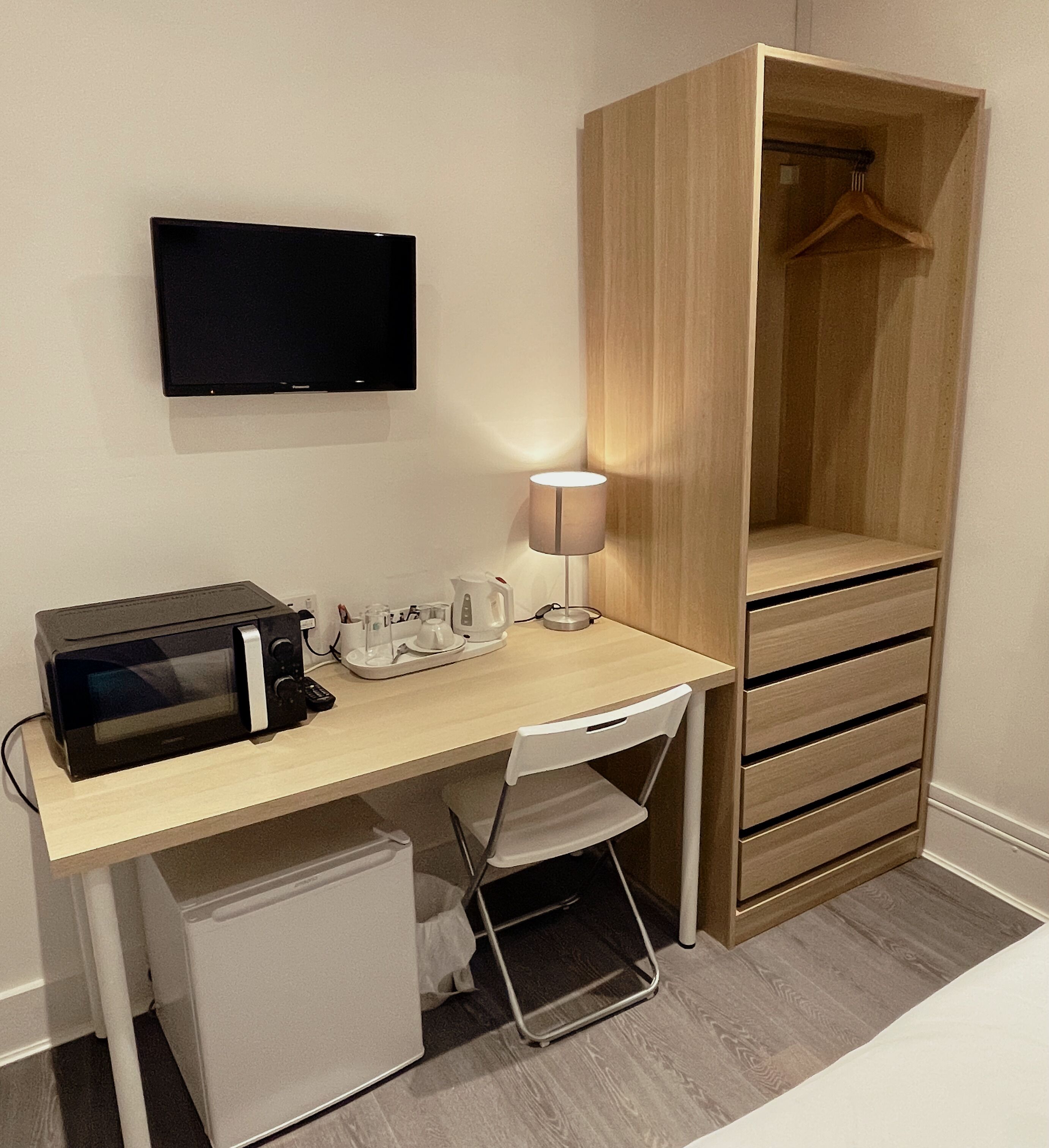 Une chambre à coucher de taille modeste, comprenant un bureau en bois, une télévision, une lampe, un four à micro-ondes et une armoire.