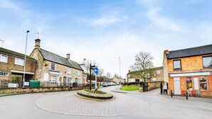 A roundabout with a cobblestone center, surrounded by brick buildings with shops and signs. - Contractor Accommodation - Cacco (Corby)