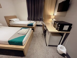 A hotel room with two beds, a desk with a microwave, a small trash bin, and a flat-screen TV mounted on the wall. - Contractor Accommodation - Cacco (Corby)