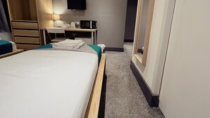 A hotel room with a bed, a desk with a computer, a TV, and a wardrobe. - Contractor Accommodation - Cacco (Corby)