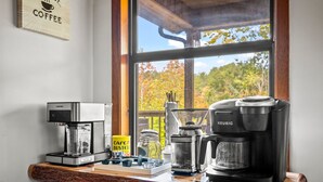 A coffee station with a Keurig and a De'Longhi coffee maker, a jar of coffee, and a 'Cafe Bustelo' mug on a wooden table by a window. - Family‑Friendly Retreat: Hot Tub, Theater + Close to Attractions (Sevierville)