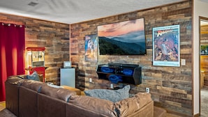 A living room with a wooden wall, a large flat-screen TV, a leather sofa, and a small table with a lamp. - Family‑Friendly Retreat: Hot Tub, Theater + Close to Attractions (Sevierville)