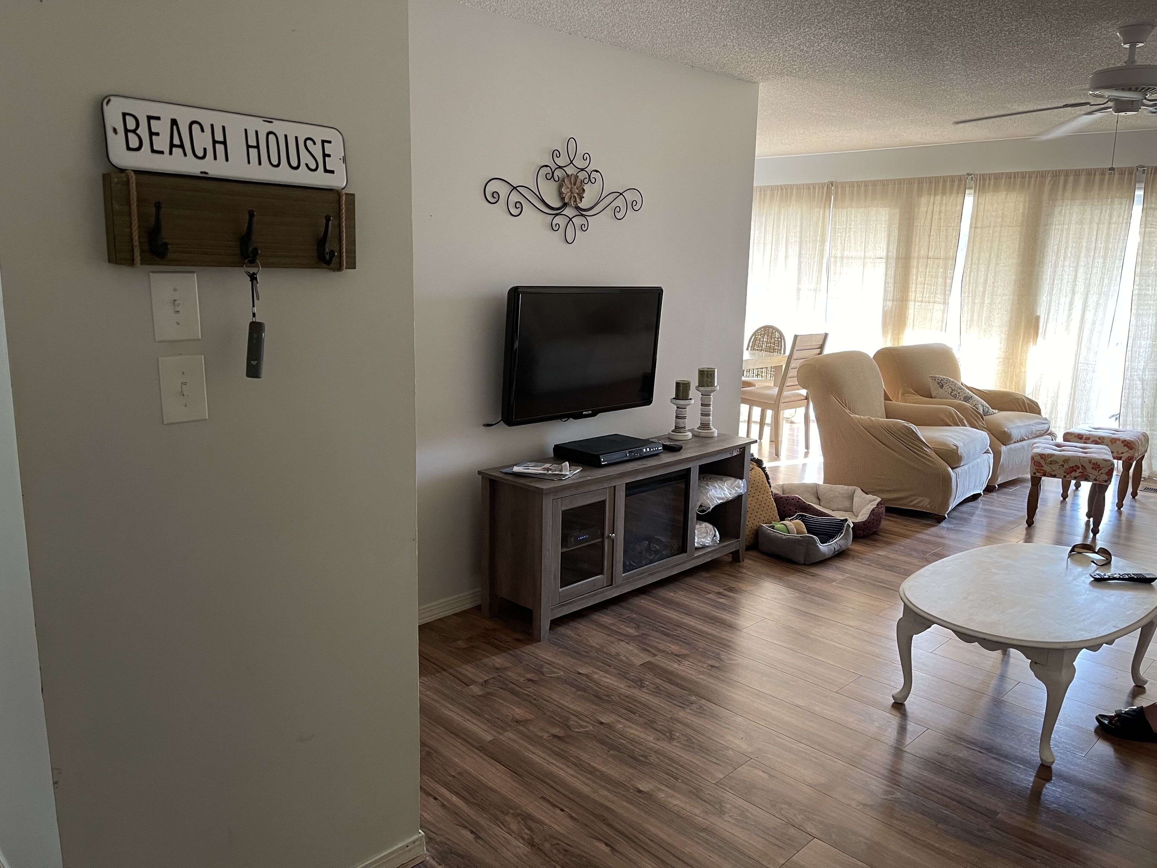 A living room with a television, a coffee table, and a sofa. There is a sign on the wall that reads "BEACH HOUSE".