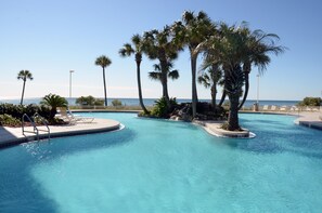 A swimming pool with palm trees and a view of the ocean. - Long Beach 1-Bedroom Condo with 2 Seasonal Beach Chairs with Umbrella (Panama City Beach)