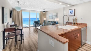 A modern kitchen with a central island, a dining area with a table and chairs, a sofa, and a view of the ocean.