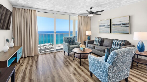 A spacious living room with a balcony, a ceiling fan, and a view of the ocean.
