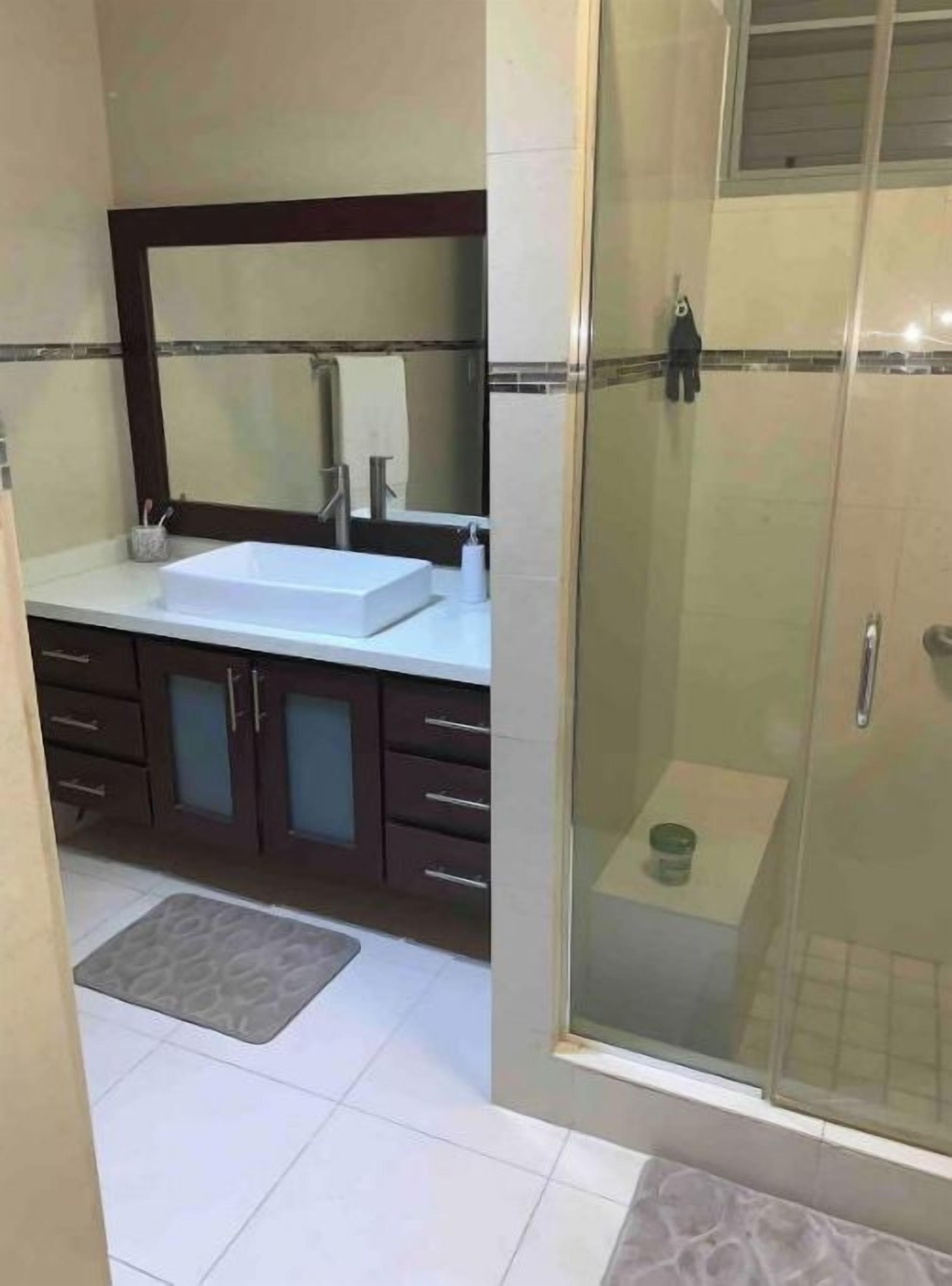 Une salle de bain avec une douche à l’italienne, un lavabo blanc et des meubles de rangement en bois foncé.