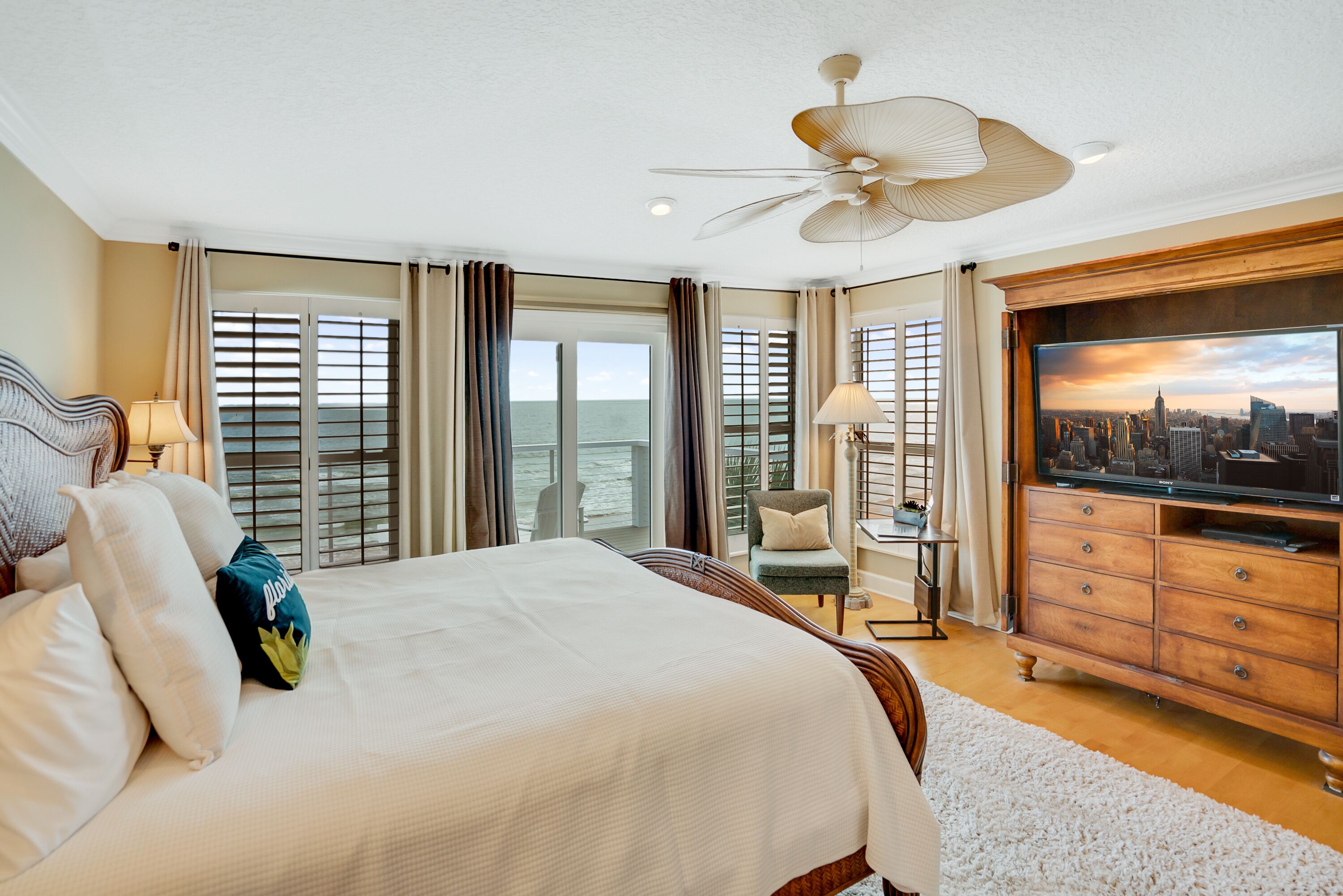 A spacious bedroom with a large bed, a television, and a view of the ocean through the windows.