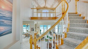 Un interior espacioso con una imponente escalera, un comedor y vista al océano.