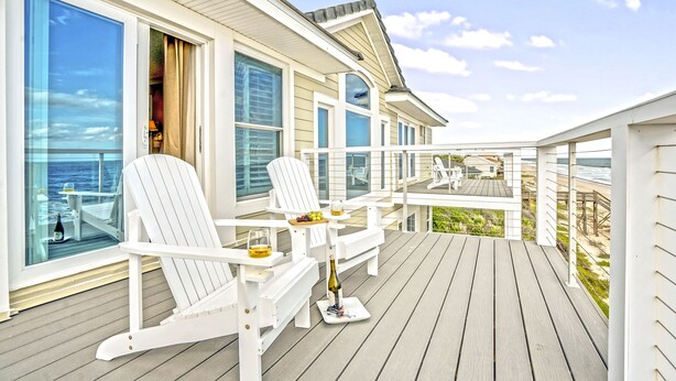 Una terrazza con poltrone Adirondack bianche, un tavolo con una bottiglia e bicchieri, e vista sull'oceano.