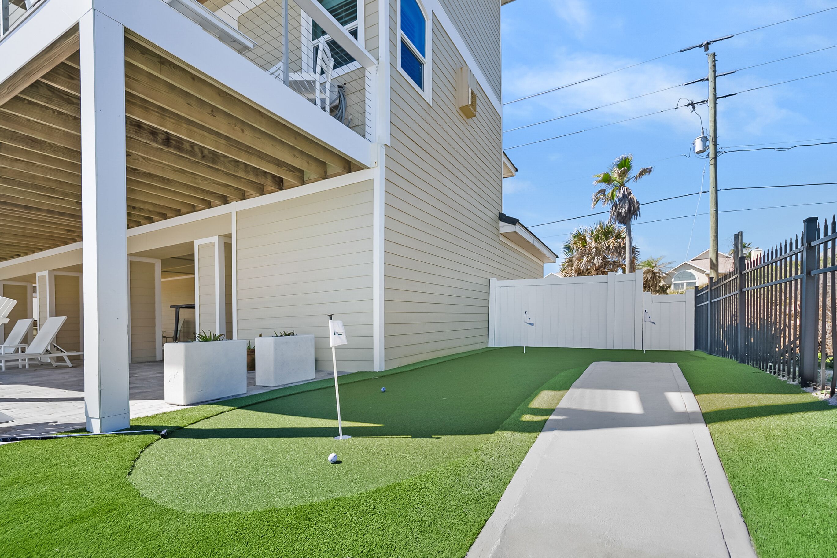 Een modern huis met een overdekte patio, een klein kunstgrasveldje en een pad dat naar het huis leidt.