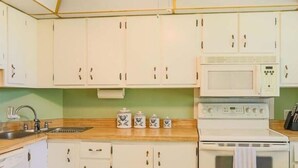 Une cuisine avec des meubles blancs, un évier en acier inoxydable, un four à micro-ondes et une cuisinière.