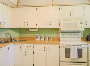 A kitchen with white cabinets, a stainless steel sink, a microwave, and a stove.